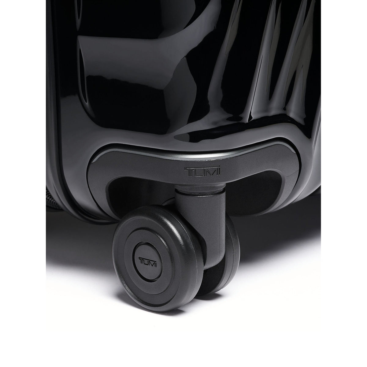 Tumi 19 Degree Continental black expandable hardside carry-on, dual spinner wheel close-up, TUMI logo on the housing